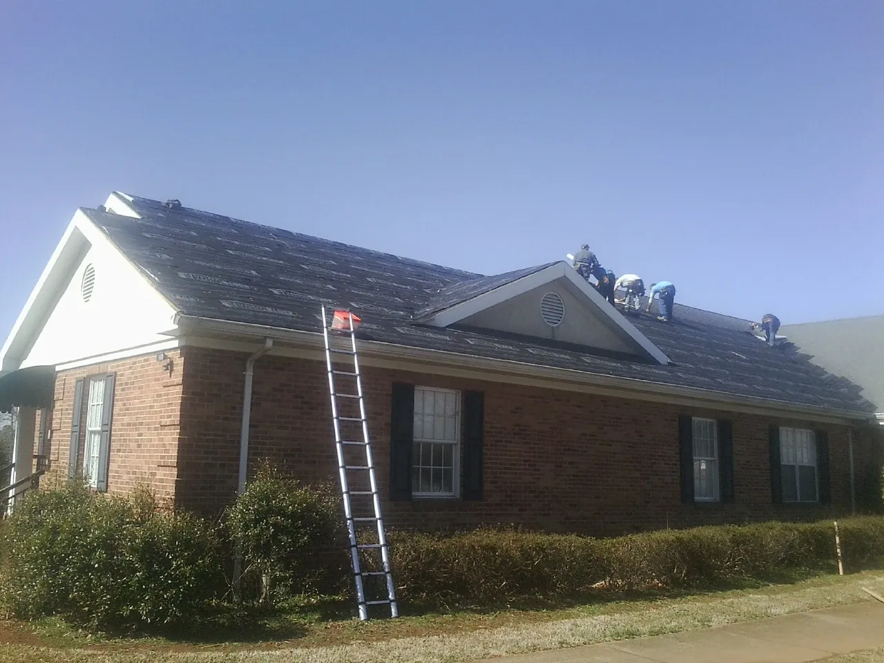 Crew tearing shingles off a brick ranch roof with a ladder set — Metal Roof Repair work by our crew in Bourbonnais