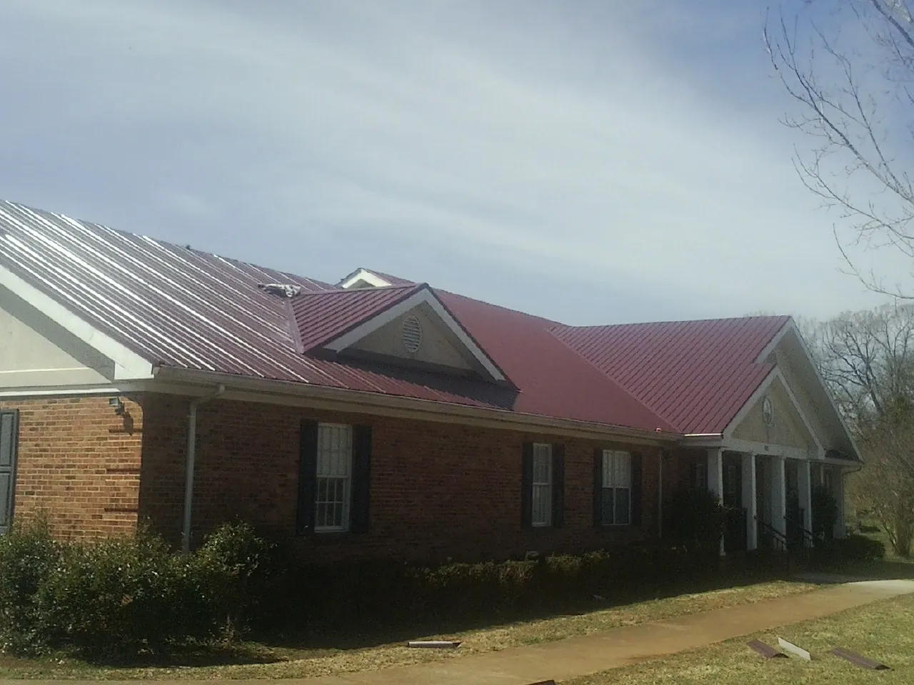 Red metal roof with gabled entries on a long brick building, from a Hail Damage Roof Repair job in Bourbonnais
