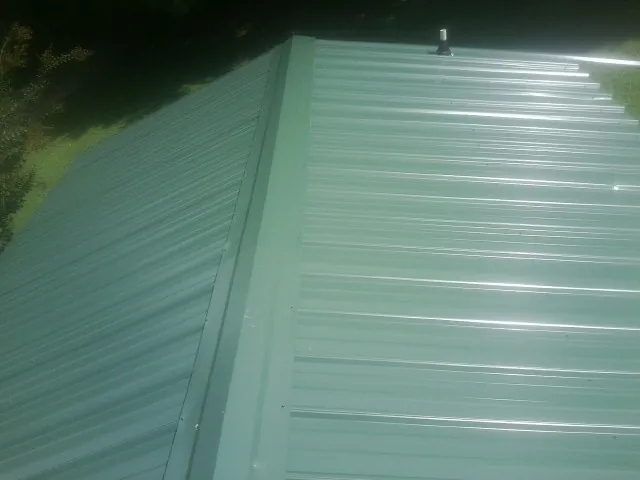 New green metal panels meeting at the ridge of a roof — Flat Roof Repair work by our crew in Bourbonnais