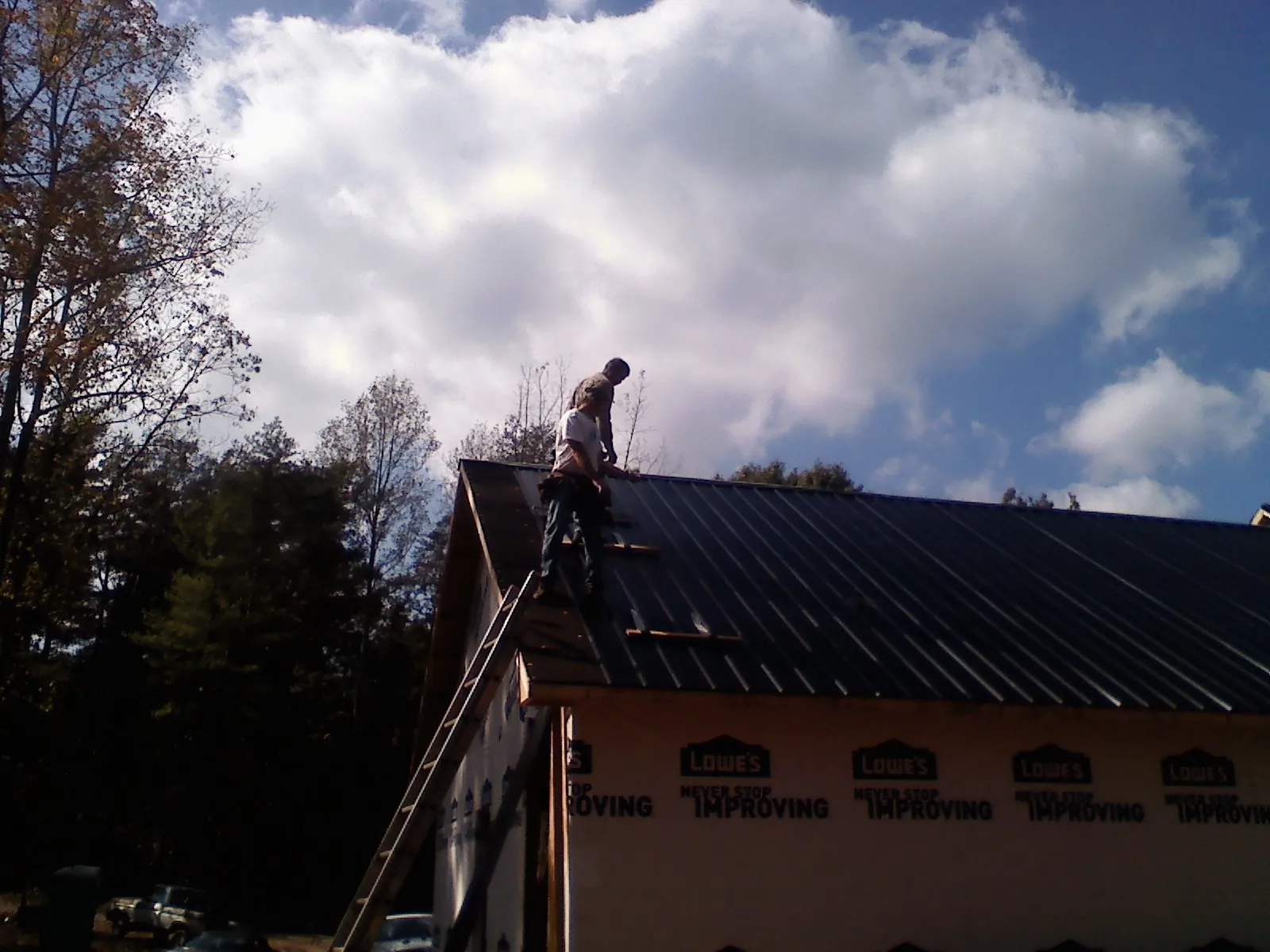 Roofer fastening dark metal panels high against a cloudy sky, from a Roof Inspection job in Bourbonnais