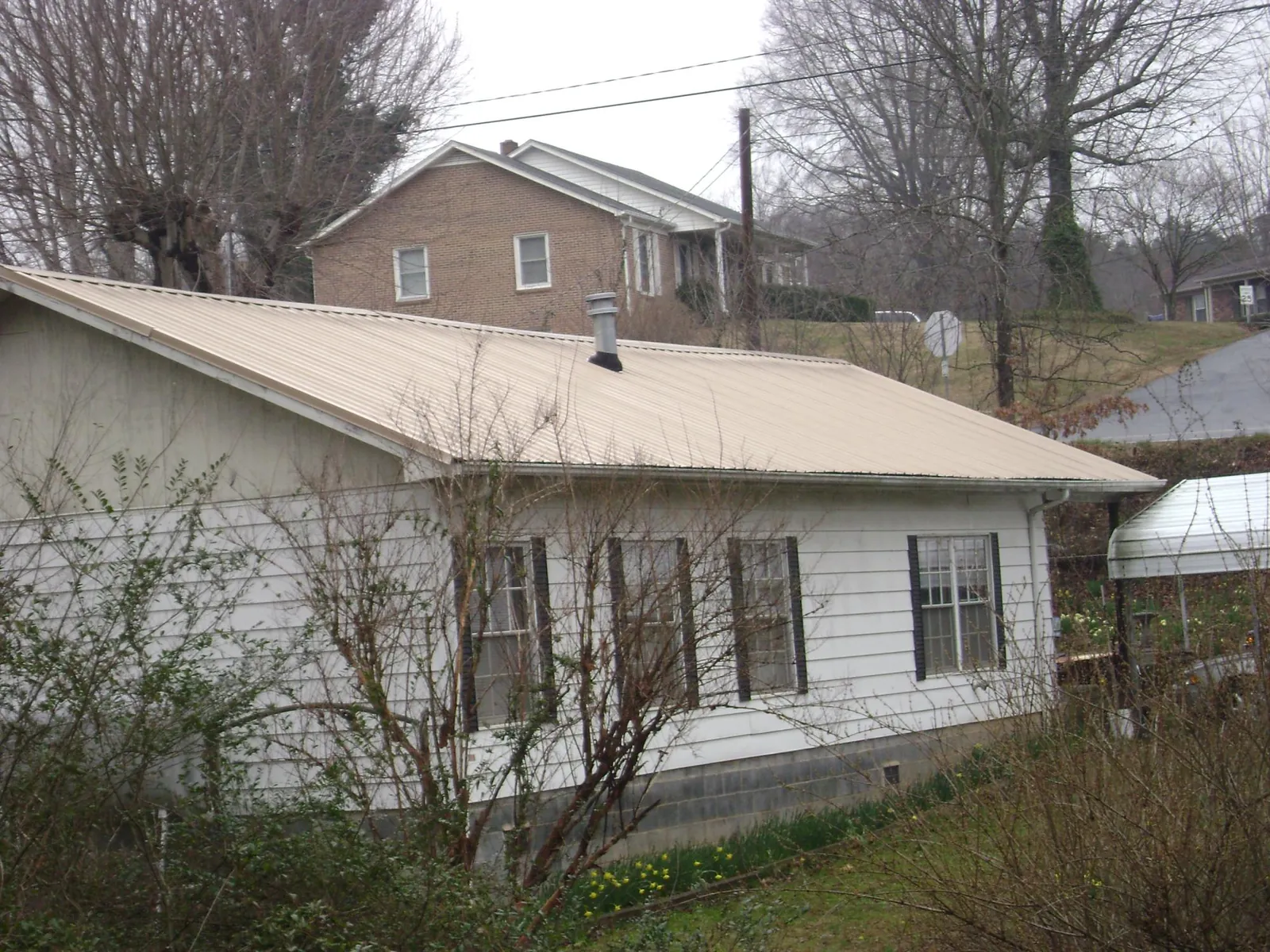 Tan metal roof on a white sided house set into a hillside — Commercial Roofing by Roofing Brothers in Bourbonnais